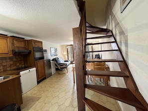 A kitchen with wooden cabinets, a dishwasher, and a microwave. There is a staircase leading to a dining area with wooden chairs and a table.