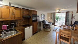 Cocina compacta con armarios de madera, lavavajillas y comedor con mesa y sillas.