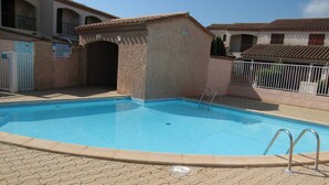 Una piscina con solárium de baldosas, un cartel que indica zona de piscina y un edificio con tejado de cerámica al fondo.