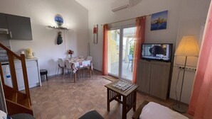 A compact living space with a dining area, a television, and a small table with a placemat. - Charming 2BR Villa with Pool, Tennis & BBQ - 200m from Beach, Saint-Cyprien (Saint-Cyprien)