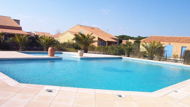 A swimming pool with tiled flooring, surrounded by buildings with red-tiled roofs and palm trees. - Charming 2BR Villa with Pool, Tennis & BBQ - 200m from Beach, Saint-Cyprien (Saint-Cyprien)