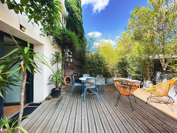 A wooden deck with blue and orange chairs, surrounded by greenery and a stone wall.