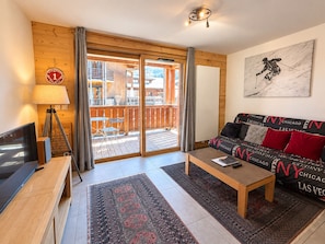 A cozy living room with a sofa, a coffee table, a TV, and a balcony with outdoor furniture. - Cozy central apartment, 1 en suite bedroom, balcony, near amenities (Les Gets)
