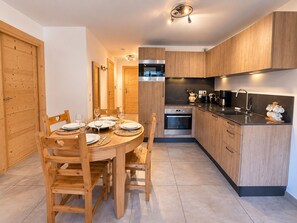 A modern kitchen with wooden cabinets, a built-in oven, and a dining area with a round table and chairs.