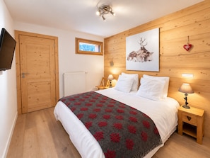 Un dormitorio con una cama, lámparas de noche, una ventana, un muro de madera y un televisor montado.