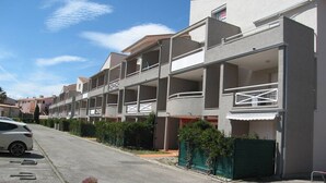 A row of modern multi-story residential buildings with balconies, a clear sky, and a parked car on the street. - Cozy 1-Bedroom Apartment with Pool, Near Beach & Port, Sleeps 5, Pet-Friendly! (Saint-Cyprien)
