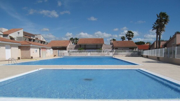 A swimming pool with a tiled deck, surrounded by buildings with red-tiled roofs. - Cozy 1-Bedroom Apartment with Pool, Near Beach & Port, Sleeps 5, Pet-Friendly! (Saint-Cyprien)
