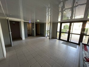 Experience the airy feel of this room with high ceilings and large windows, featuring a potted plant and tiled floor.