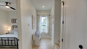 A narrow hallway with a bed, a sofa, and a door leading to a bright room. - Galveston Modern - 4BR with Panoramic Views (Galveston)