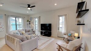 A modern living room with a sofa, a TV, a wooden chair, and a small table. - Galveston Modern - 4BR with Panoramic Views (Galveston)