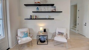 A modern living room with two white armchairs, a coffee table, and three black floating shelves with decorative items. - Galveston Modern - 4BR with Panoramic Views (Galveston)
