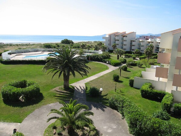 A resort with a swimming pool, palm trees, and a view of the sea.