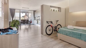 A modern hotel room with a bed, a bicycle, a desk, and a view of the dining area. - Living Siena - Apartment "Strade Bianche" (Siena)
