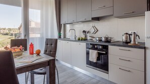 A modern kitchen with grey cabinets, a black stove, and a dining area with a table and chairs. - Living Siena - Apartment "Strade Bianche" (Siena)