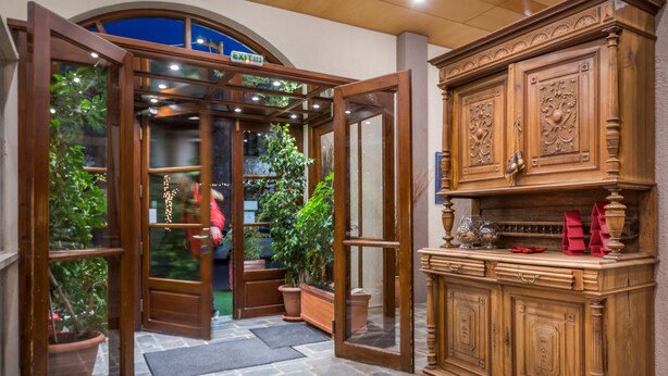 A wooden cabinet with intricate carvings, a stone-tiled floor, and a glass door leading to a room with a view of greenery.
