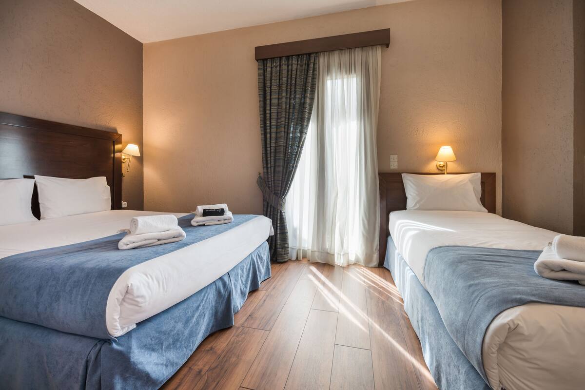 Ein Hotelzimmer mit zwei Betten, Holzboden und einem Fenster mit Vorhängen.