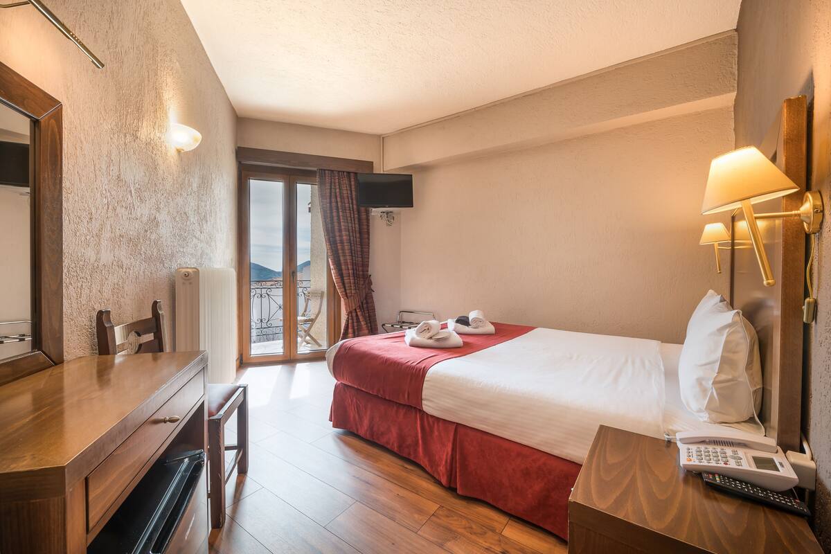 Ein Hotelzimmer mit Bett, Schreibtisch, Stuhl, Telefon und Fernseher.