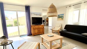 Een ruime woonkamer met een bank, een salontafel, een televisie en een eethoek op de achtergrond.