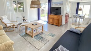 Een ruime woonkamer met een bank, stoelen, een televisie en een eettafel.