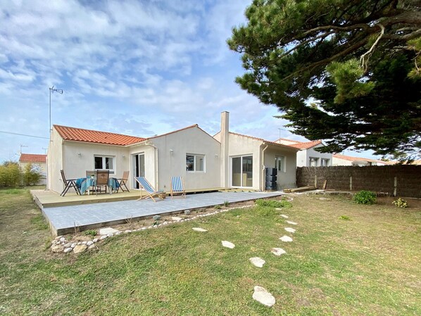 A two-story house with a tiled roof, a patio with outdoor furniture, and a grassy yard with stepping stones.