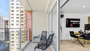 A balcony with a dining table and chairs, a TV mounted on the wall, and a view of a high-rise building. - InCity Charming Studio (Bucharest)