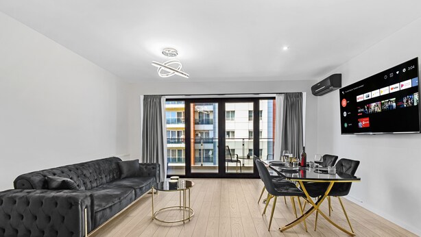 A modern living room with a black sofa, a glass coffee table, and a dining area with a black table and gold chairs. - InCity Charming Studio (Bucharest)