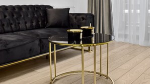 A modern living room with a black sofa, a gold-framed side table, and a window with sheer curtains. - InCity Charming Studio (Bucharest)
