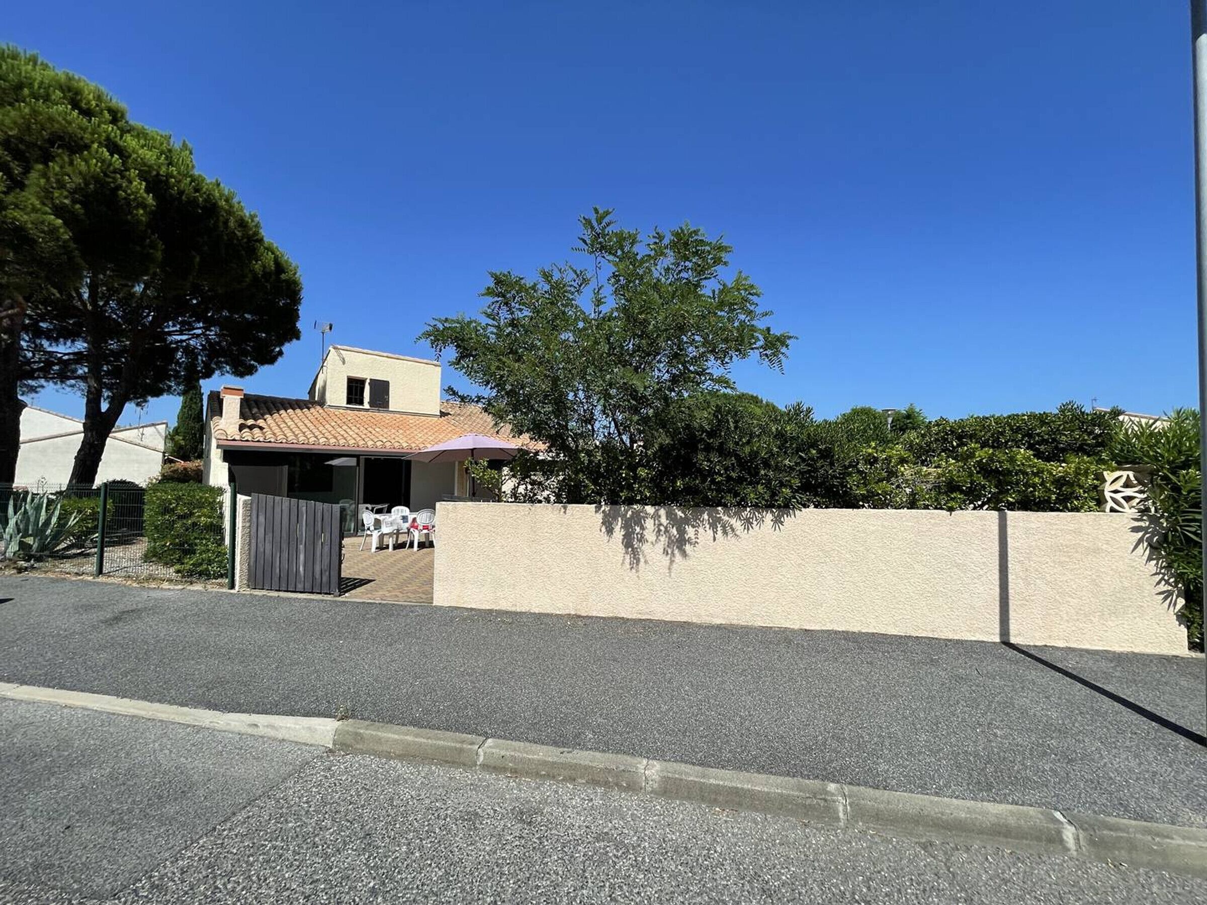 Une propriété résidentielle dotée d’un patio couvert, d’un jardin clôturé et offrant une vue sur un ciel bleu dégagé.