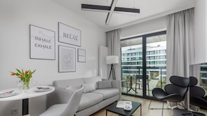 Ein modernes Wohnzimmer mit grauem Sofa, schwarzen Sesseln, einem Couchtisch und einem Essbereich mit weißem Tisch und Tulpen.