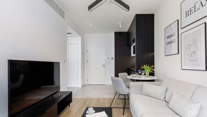 Ein modernes Wohnzimmer mit Flachbildfernseher, einer Couch, einem Couchtisch mit einer Zeitschrift und einem Essbereich mit Tisch und Stühlen.