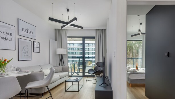 Ein modernes Wohnzimmer mit Sofa, Couchtisch und TV-Möbel. Es gibt einen Essbereich mit Tisch und Stühlen. Das Zimmer hat große Fenster mit Vorhängen und Blick auf Gebäude.