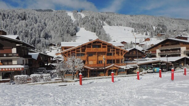 A snow-covered village with wooden buildings, including a large hotel with balconies and a sign for a restaurant.