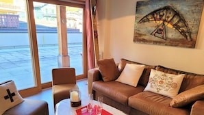 A living room with a leather sofa, a glass coffee table, and a view through large windows.