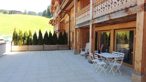 A wooden building with a balcony, outdoor seating area, and a view of a green landscape.