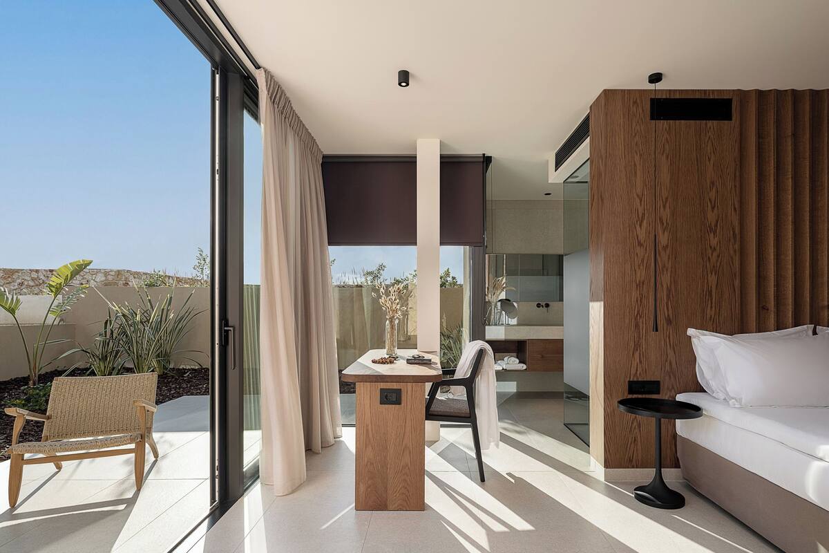 A modern, well-lit room with a glass door leading to an outdoor area, a wooden table with a vase, a sofa, and a small side table.