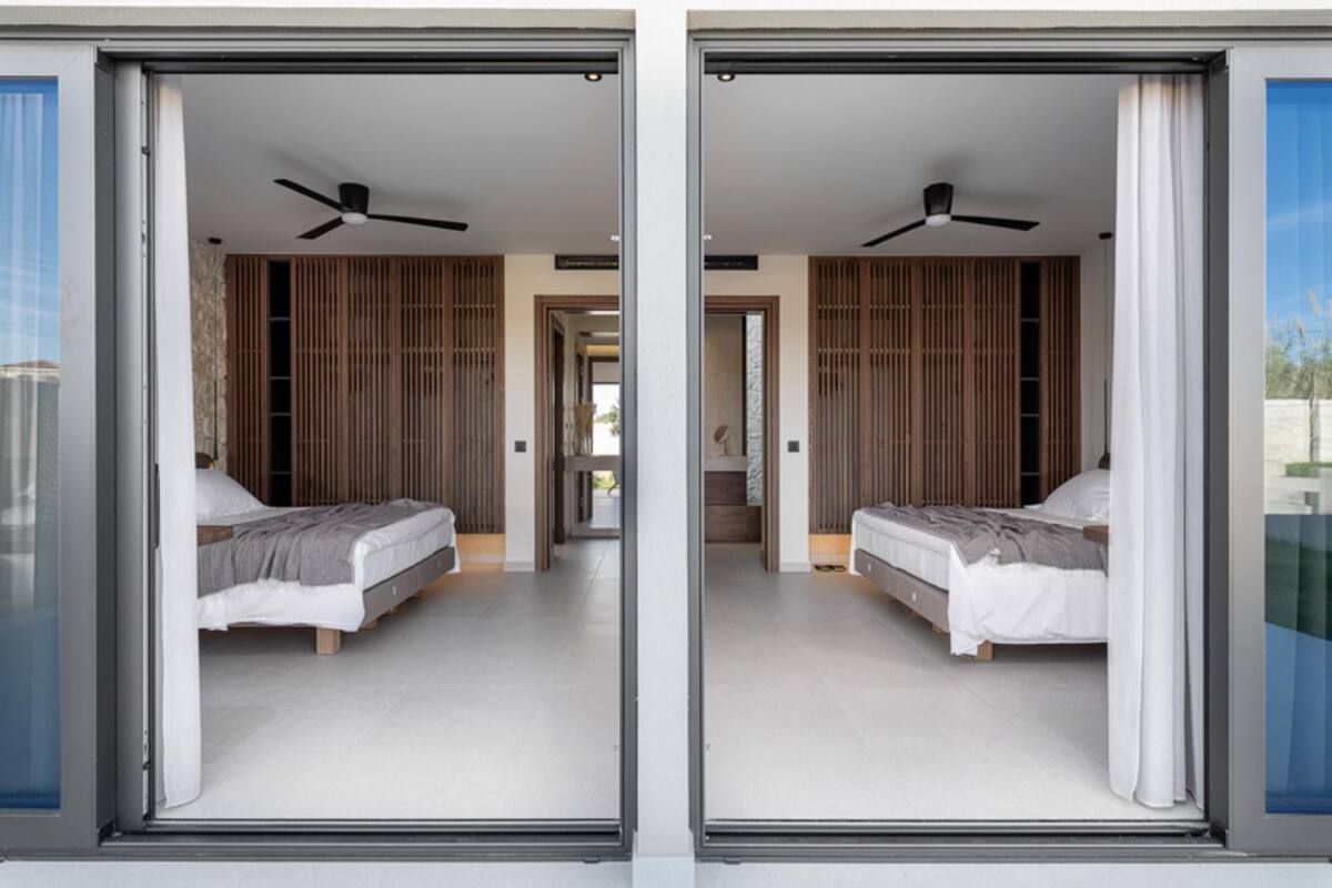 A modern bedroom with two beds, a ceiling fan, and a sliding glass door leading to a balcony.