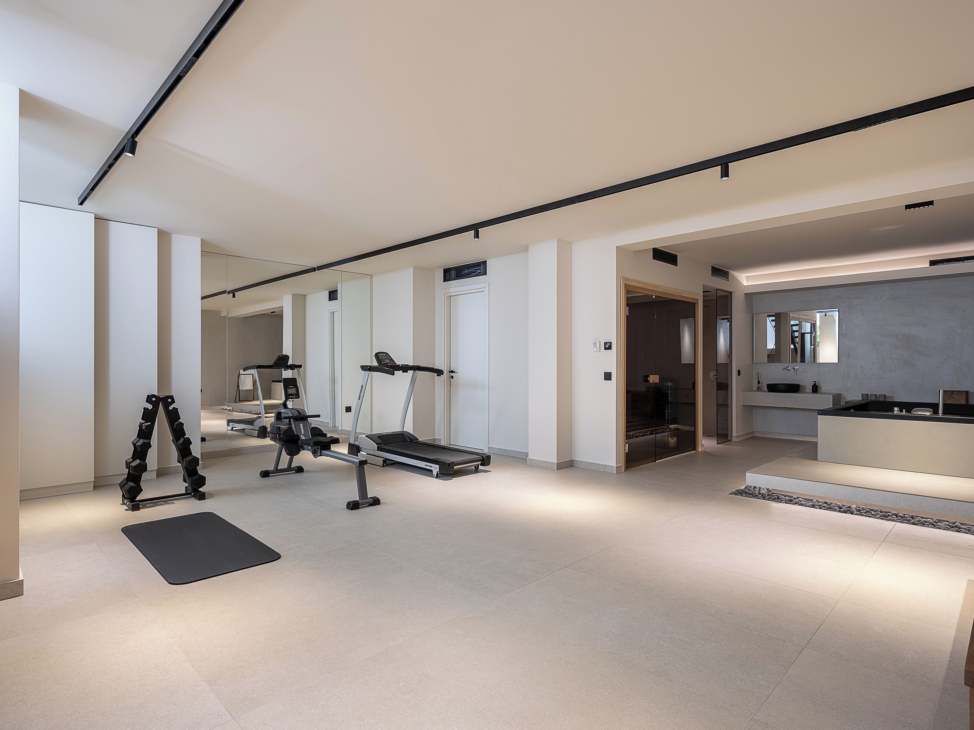 A modern hotel room with a gym area, a large mirror, and a minimalist bathroom.