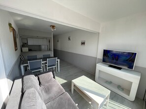 A compact living space with a sofa, a TV, a dining area, and a kitchenette. - Two-room apartment, 4 beds, near the port and beach, with parking and park view, pet-friendly (Saint-Cyprien)