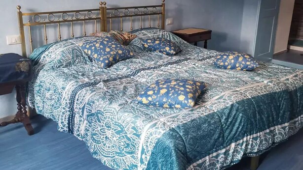A bed with a patterned bedspread and pillows, a wooden headboard, and a small bedside table. - Apartment in the center of Sagliano Micca (Sagliano Micca)
