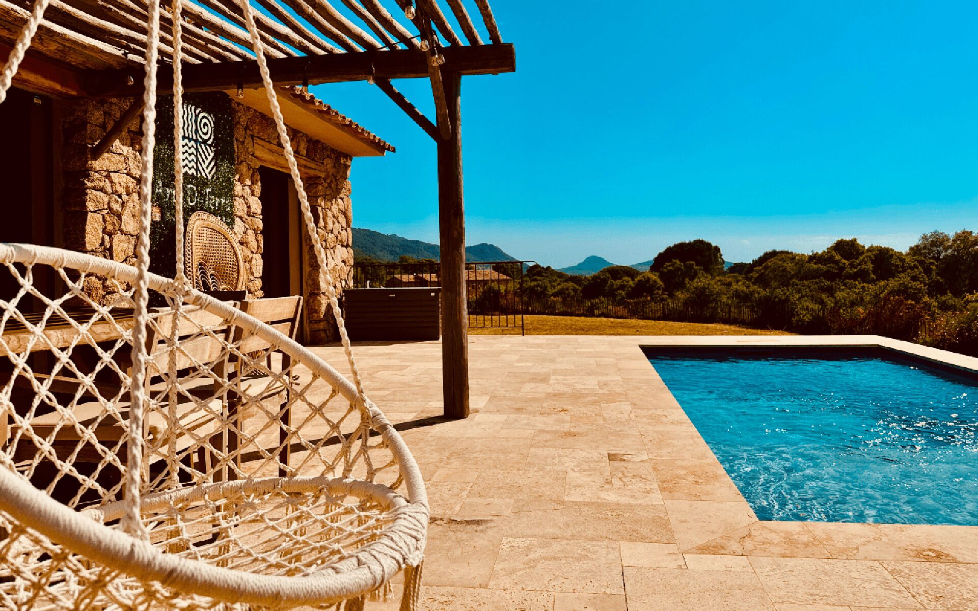 A stone building with a pool, a rope chair, and a view of the mountains.