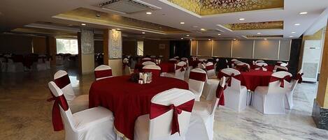 Un salón de banquetes con mesas redondas cubiertas con manteles rojos y sillas blancas adornadas con cintas rojas.