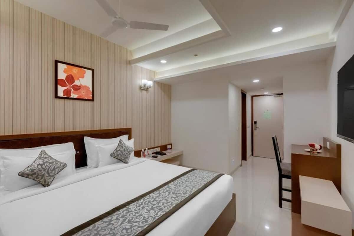 Ein Hotelzimmer mit einem großen Bett, einem Schreibtisch, einem Sessel, einem Deckenventilator und einem Bild an der Wand.