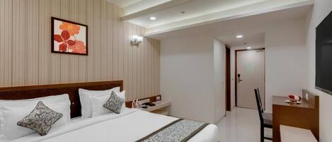 Habitación de hotel con una cama grande, un escritorio, una silla, un ventilador de techo y un cuadro en la pared.