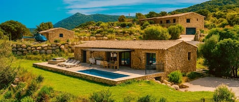 A stone villa with a swimming pool, outdoor seating, and a view of the surrounding hills.
