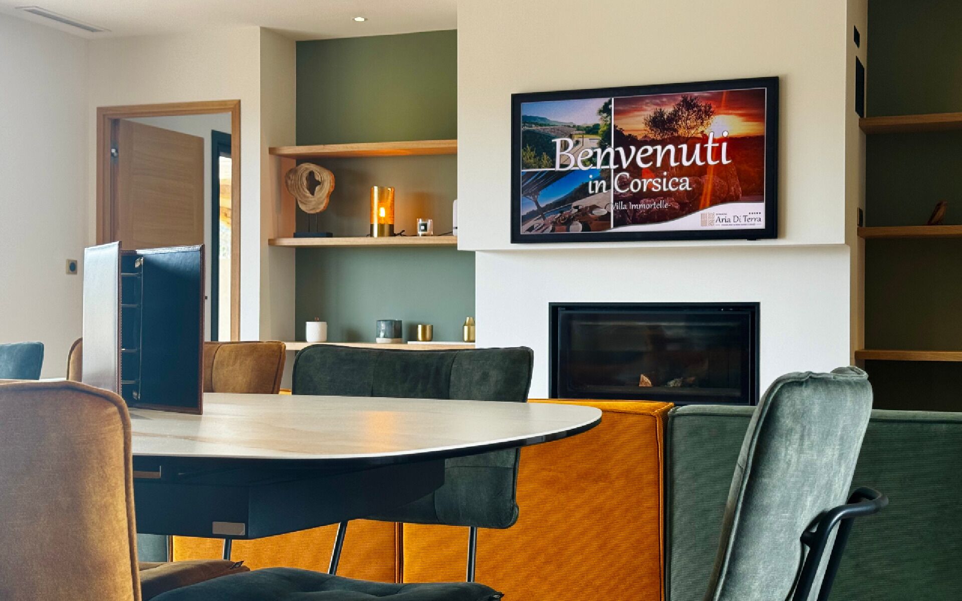 Habitació d'hotel moderna amb una taula de dinar rodona, seients còmodes, una llar de foc i un cartell de benvinguda emmarcat.