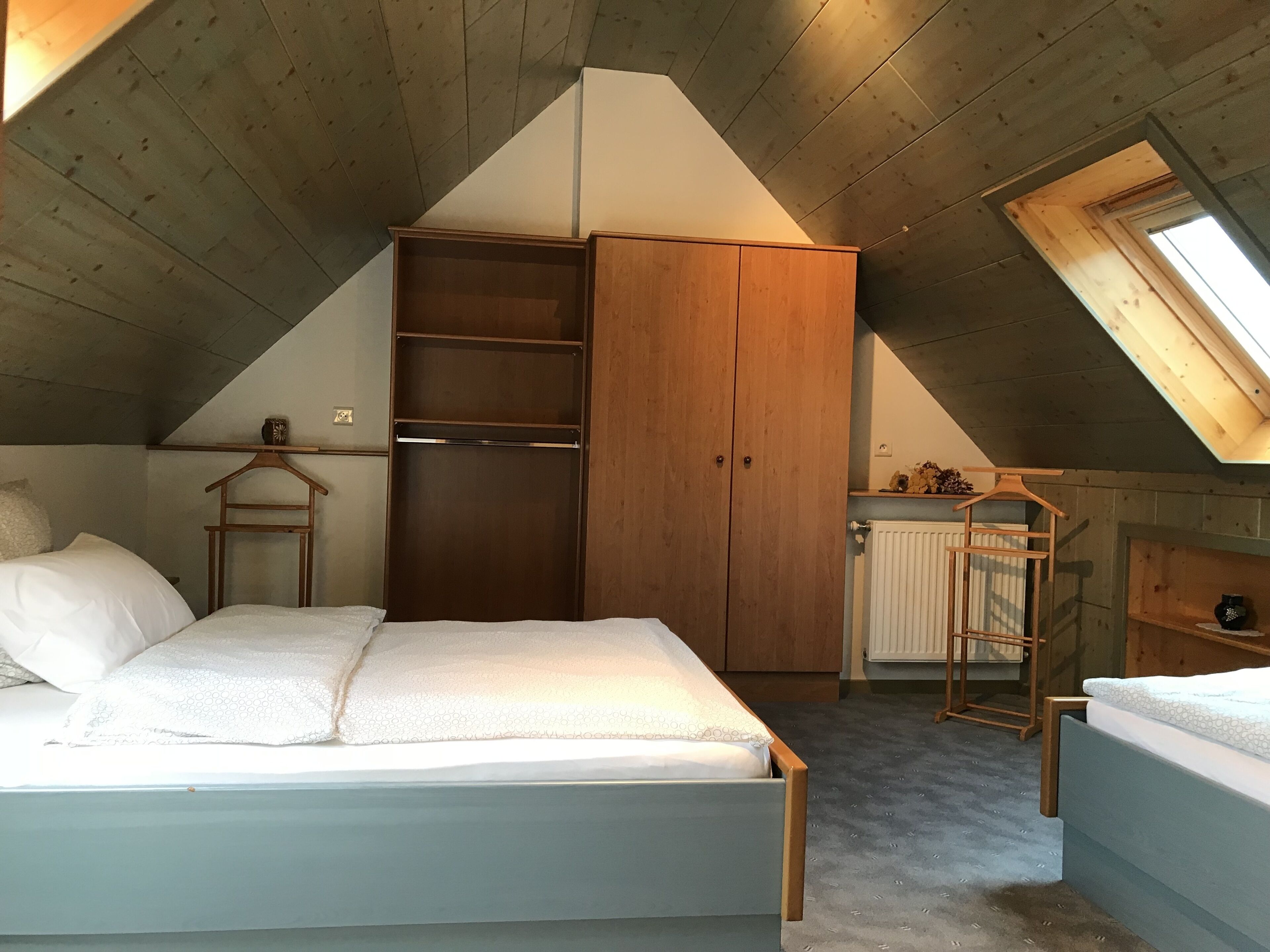 Camera da letto con soffitto spiovente, armadio in legno e una piccola finestra.