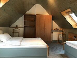 A bedroom with a sloped ceiling, wooden wardrobe, and a small window. - 5-person apartment (Soultzmatt)