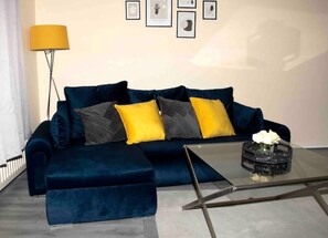 Relax in this stylish living room with a dark blue sofa, glass coffee table, and a vase with a single white flower.