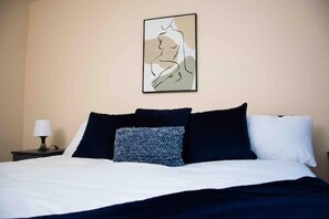 Restful retreat with a neatly made bed and a bedside lamp, complemented by a unique piece of art above.