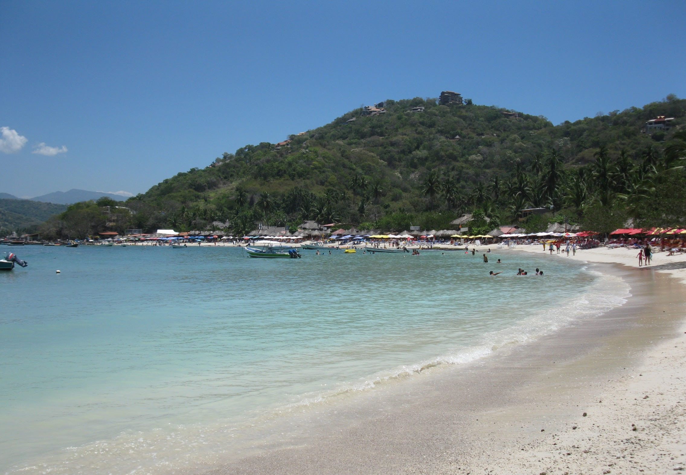 Une plage avec une eau cristalline, des bateaux et des parasols.